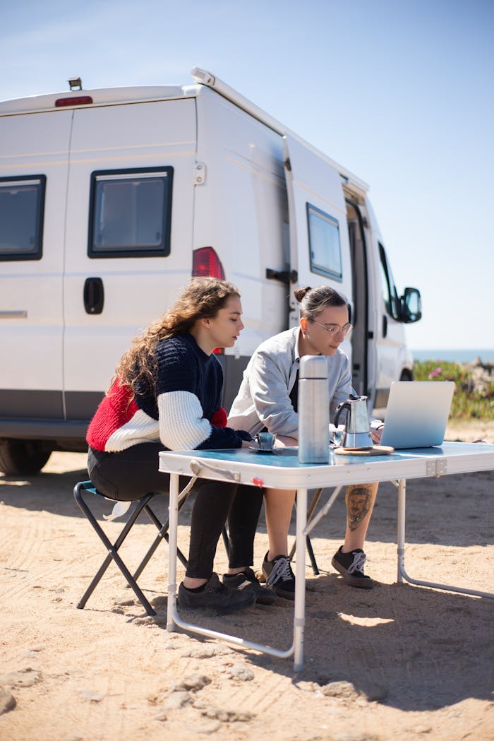 A couple enjoying remote work on a laptop while traveling in a camper van with an ocean view in Portugal.